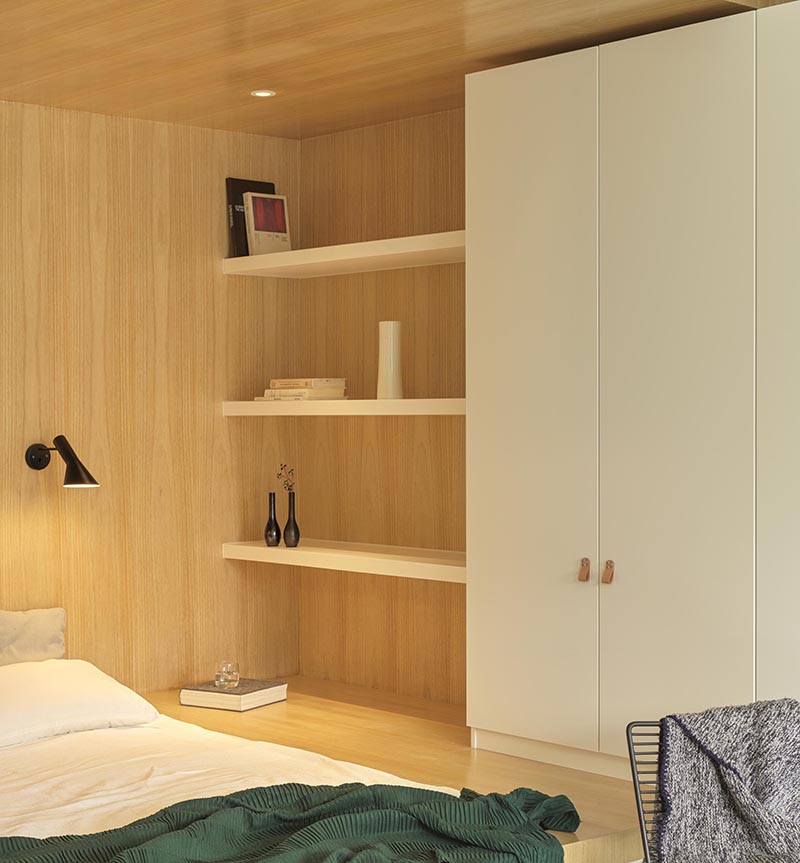 Au lieu d'avoir un lit autoportant, les concepteurs ont utilisé un petit coin de forme étrange positionné le lit dans la base de sa propre niche bordée de bois, permettant plus d'espace au sol grâce aux grandes fenêtres. #BedroomIdea #BedNook #BedNiche #BuiltInBed #InteriorDesign #ModernBedroom #Shelving