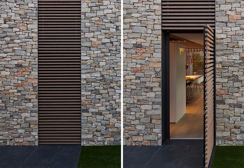 Cette maison moderne a un détail de lattes de bois qui fournit non seulement un intérêt visuel sur la façade, mais elle cache également une porte qui s'ouvre sur l'intérieur de la maison. #WoodSlat #Facade #ModernHouse #StoneHouse #WoodAccent #Architecture #Doors