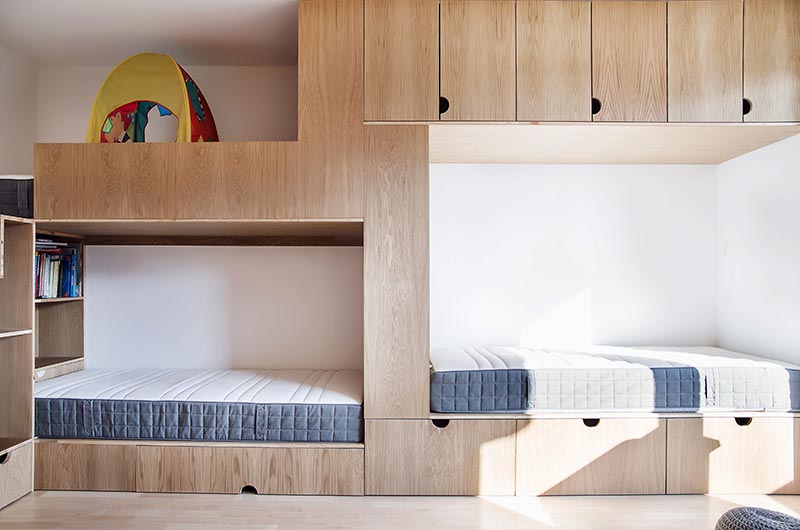 Cette chambre d'enfant moderne a de hauts plafonds, une porte coulissante en bois, un espace ouvert pour jouer, un mur d'armoires et un lit superposé conçu pour trois. #BunkBed #KidsRoom #ChildrensBedroom #Cabinets #BedDesign