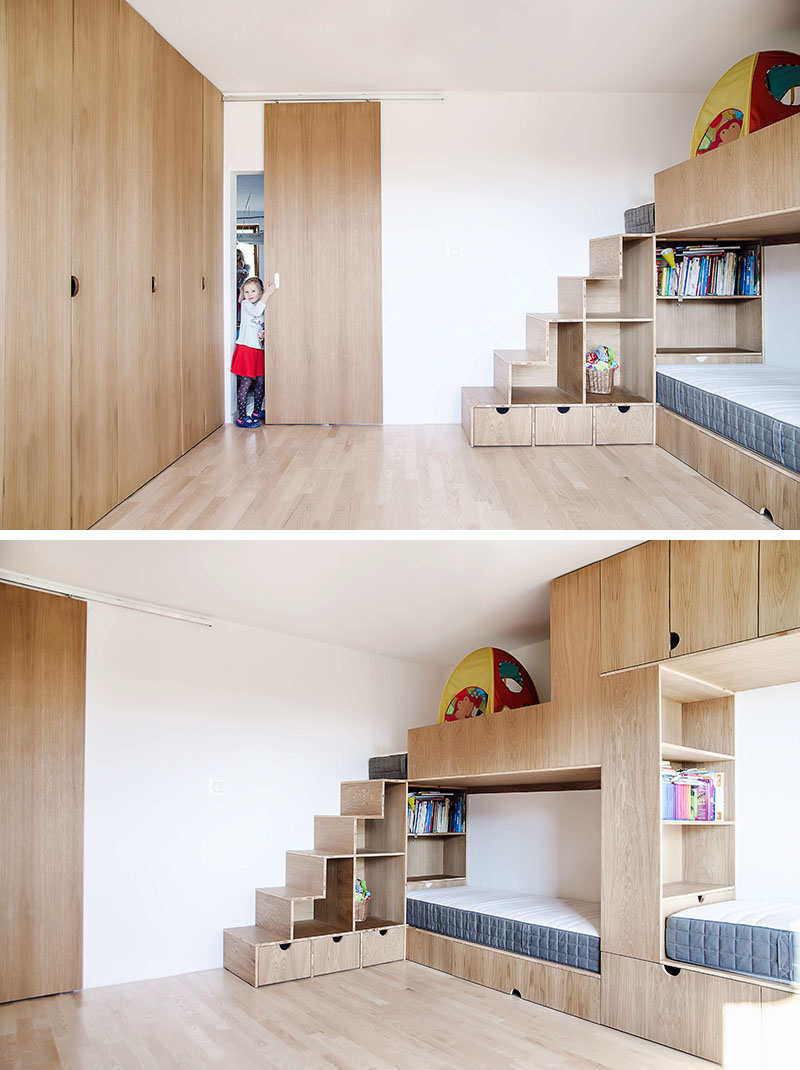 Cette chambre d'enfant moderne a de hauts plafonds, une porte coulissante en bois, un espace ouvert pour jouer, un mur d'armoires et un lit superposé conçu pour trois. #BunkBed #KidsRoom #ChildrensBedroom #Cabinets #BedDesign