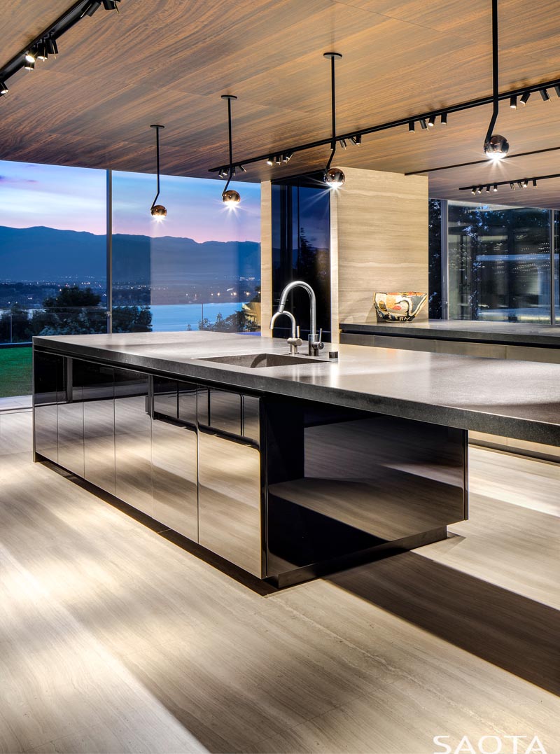 Le plafond en bois de cette cuisine moderne ajoute de la chaleur, tandis que les armoires de l'îlot de cuisine ont une finition miroir. #KitchenDesign #MirroredCabinets