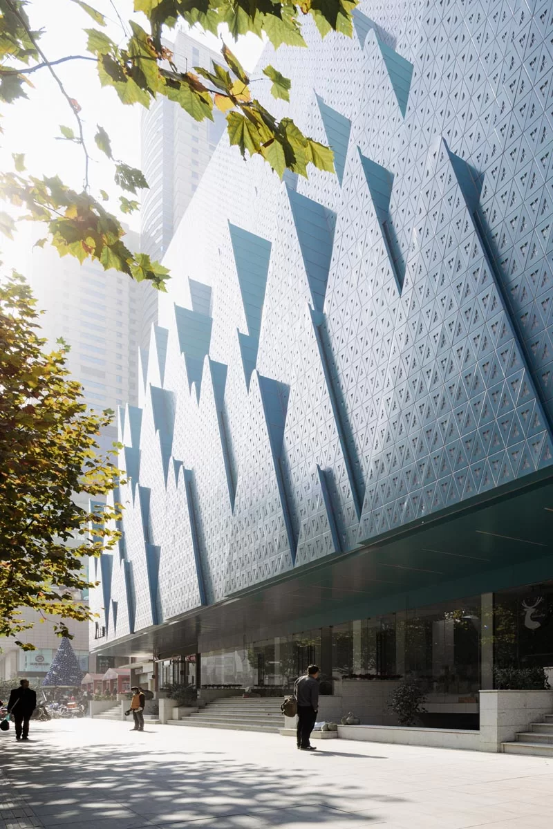 Des couches de plaques d'aluminium perforées en forme de montagnes ont été conçues pour créer un arrière-plan pour les arbres de la rue et symboliser la nouvelle vie de la librairie de langues étrangères du Hubei. #Architecture #FacadeDesign #BuildingDesign