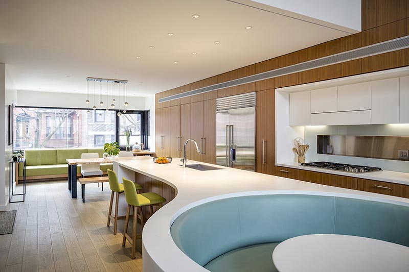 Le comptoir de l'île Corian blanc sur mesure dans cette cuisine moderne, a une forme rectangulaire à une extrémité, avant de passer à une conception incurvée divisée qui s'enroule autour des banquettes bleu doux qui composent le coin petit-déjeuner intégré. #KitchenDesign #ModernKitchen #BreakfastNook #BanquetteSeating #KitchenIsland
