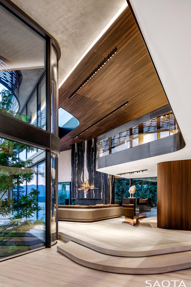 Ce salon moderne à double hauteur a un plafond en bois avec éclairage d'accentuation, tandis qu'un mur en pierre noir et blanc ajoute à la sensation de hauteur avec ses lignes verticales. #LivingRoom #StoneWall #WoodCeiling #ModernInterior