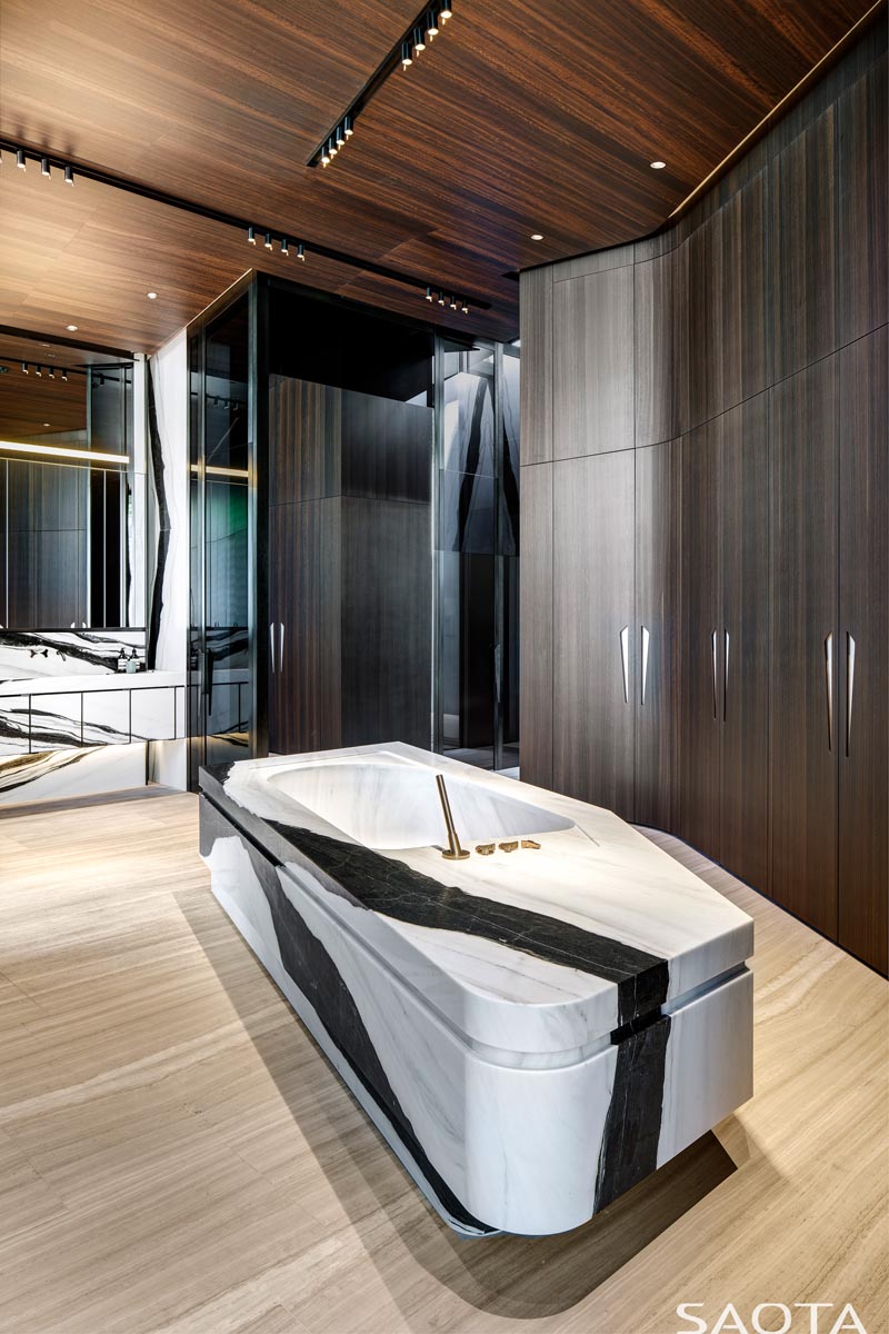 Dans cette salle de bain moderne, de hauts placards en bois bordent le mur, tandis qu'une baignoire en pierre est située au centre. #ModernBathroom #BathroomDesign #StoneBathtub