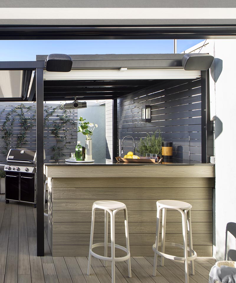 Cette terrasse extérieure moderne dispose d'un bar avec des sièges. Un détail caché est l'écran blanc qui peut être abaissé pour afficher un film. #Terrace #OutdoorBar #Projector
