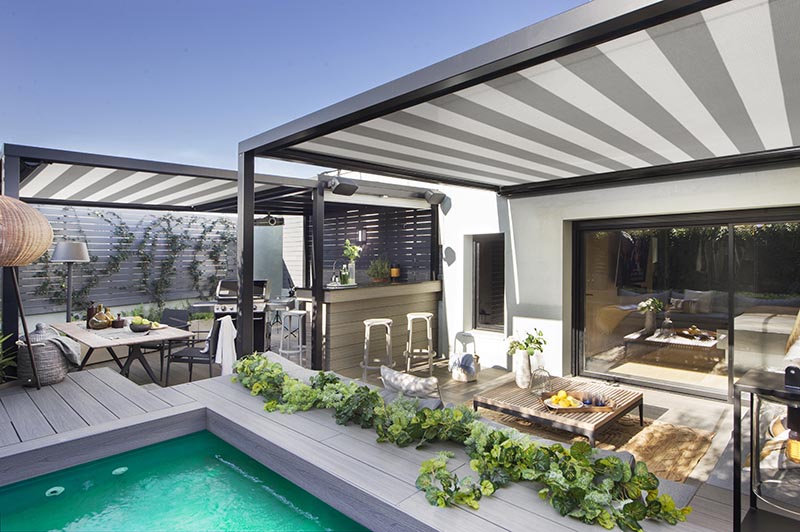 Cette terrasse moderne a des toiles d'ombrage avec un motif rayé qui ajoutent un autre élément de design à l'espace, complétant les accents noirs et gris utilisés dans tout l'espace extérieur. #ShadeClothes #Terrace #Outdoor Entertaining #SwimmingPool
