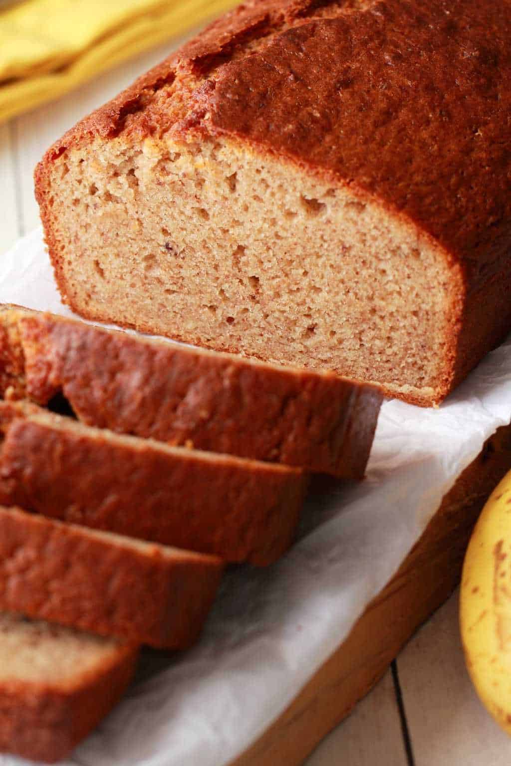 Une miche de pain aux bananes végétalien en tranches sur du papier sulfurisé.