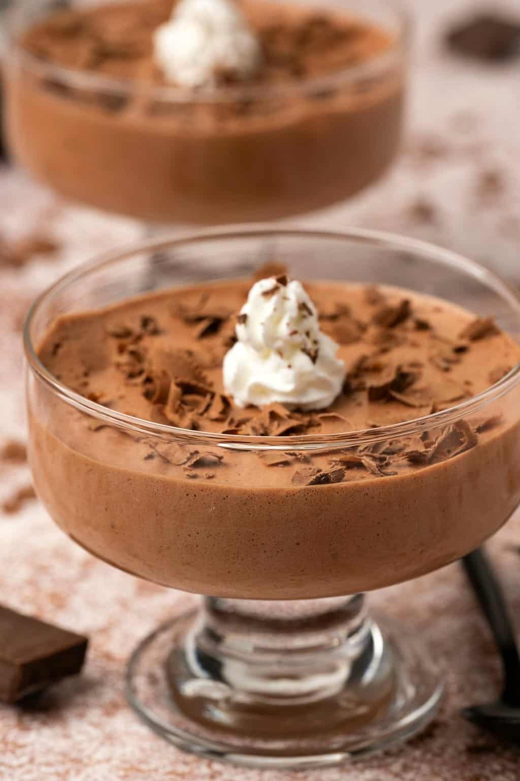 Mousse végétalienne dans des plats de service en verre avec de la crème fouettée et des copeaux de chocolat.