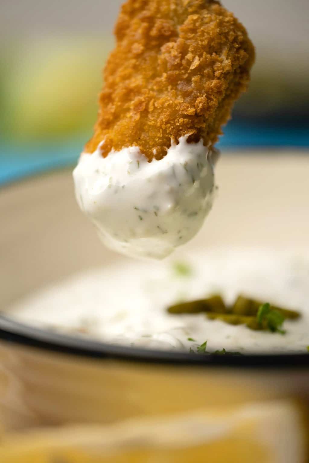 Pépite végétalienne trempant dans un bol de sauce tartare.