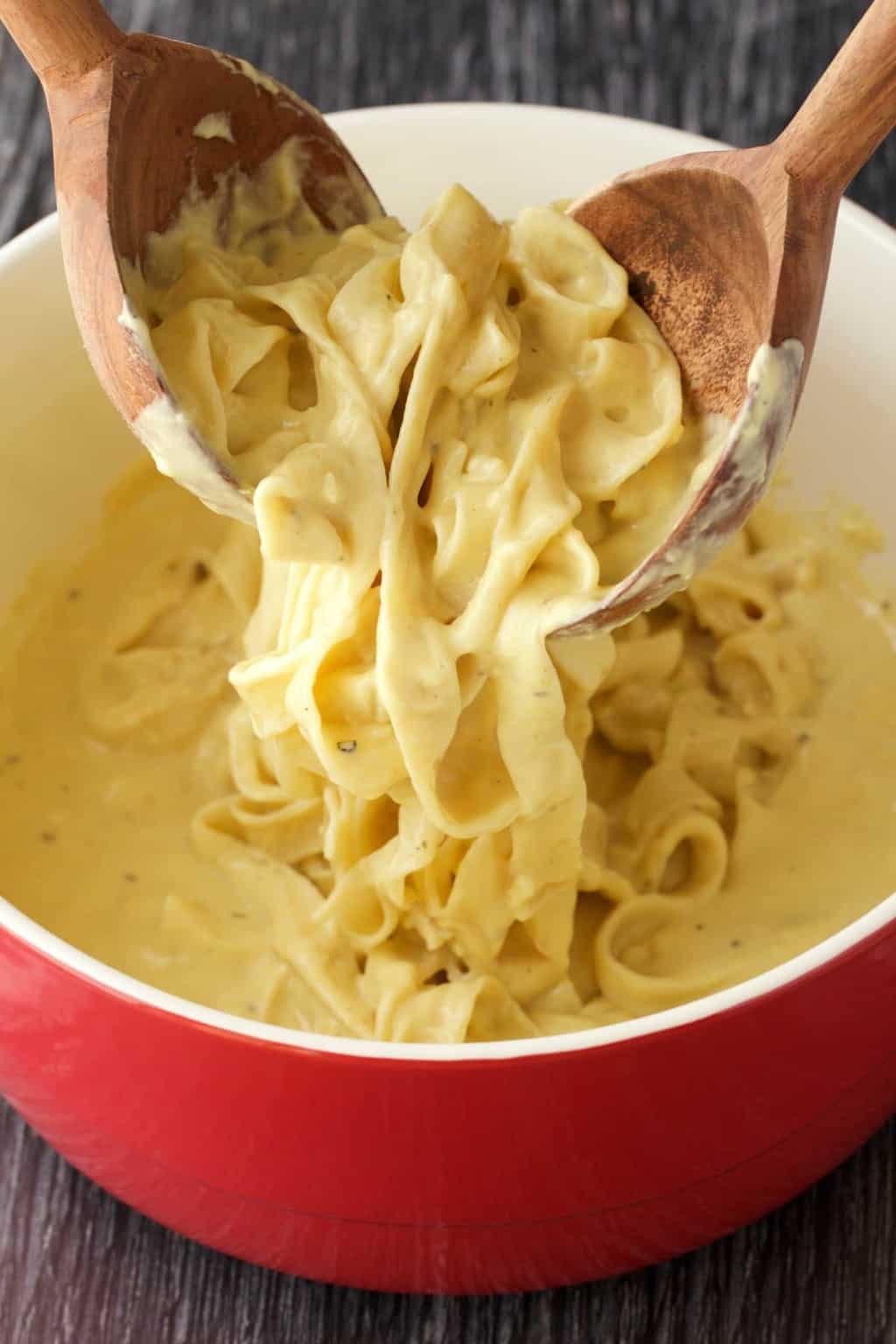 Mélanger de la fettucine végétalienne alfredo dans un plat de service rouge et blanc.