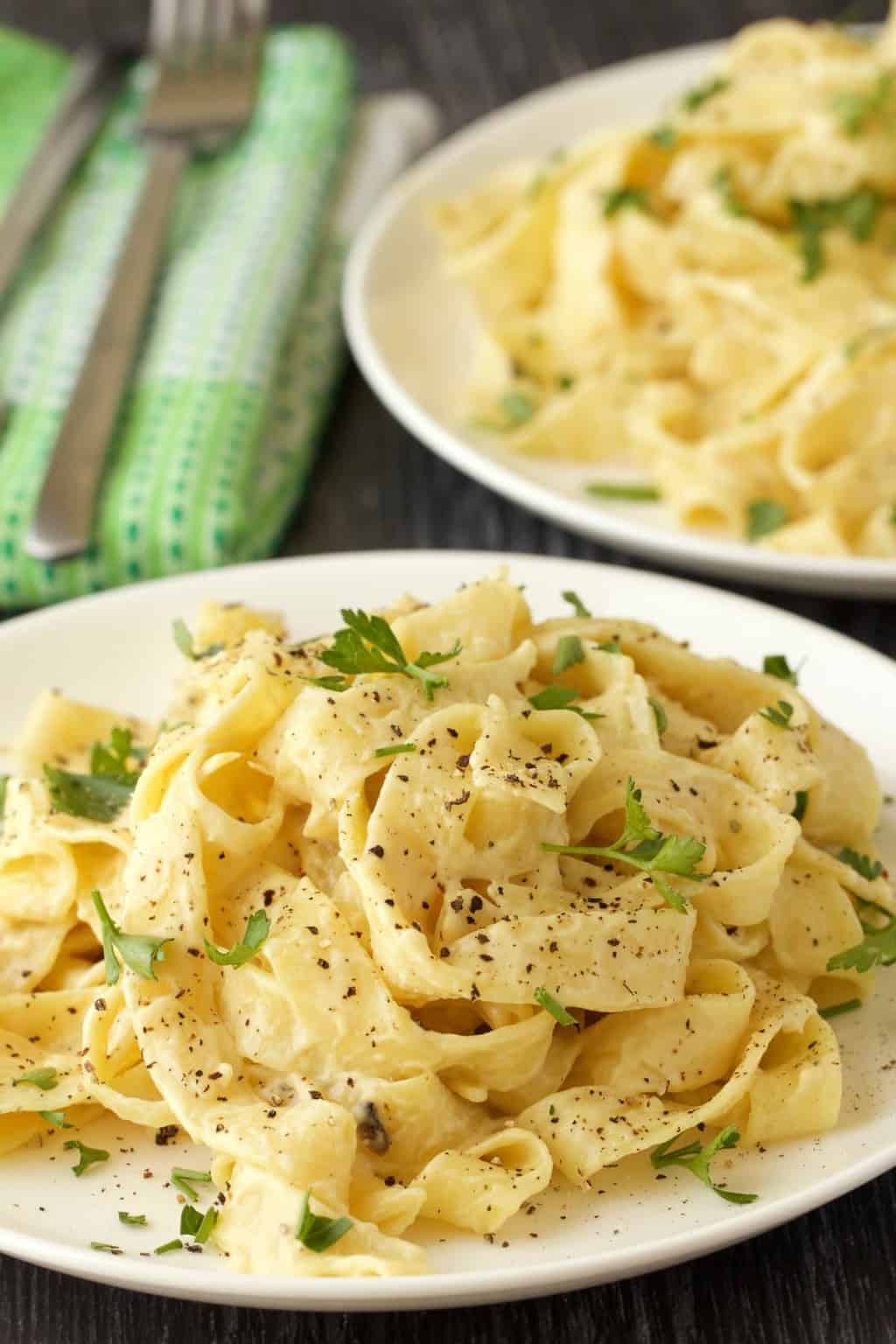 Fettucine alfredo végétalienne avec du persil frais et du poivre noir sur une plaque blanche.