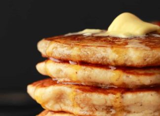 Crêpes végétaliennes – légères, moelleuses et parfaites Une pile de crêpes végétaliennes avec du beurre fondu sur le dessus et du sirop qui coule sur les côtés.