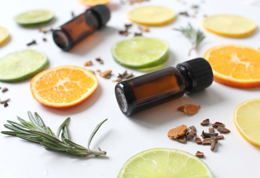 petites bouteilles d'huile essentielle brune entourées de tranches d'orange, de lime, de graines et d'herbes