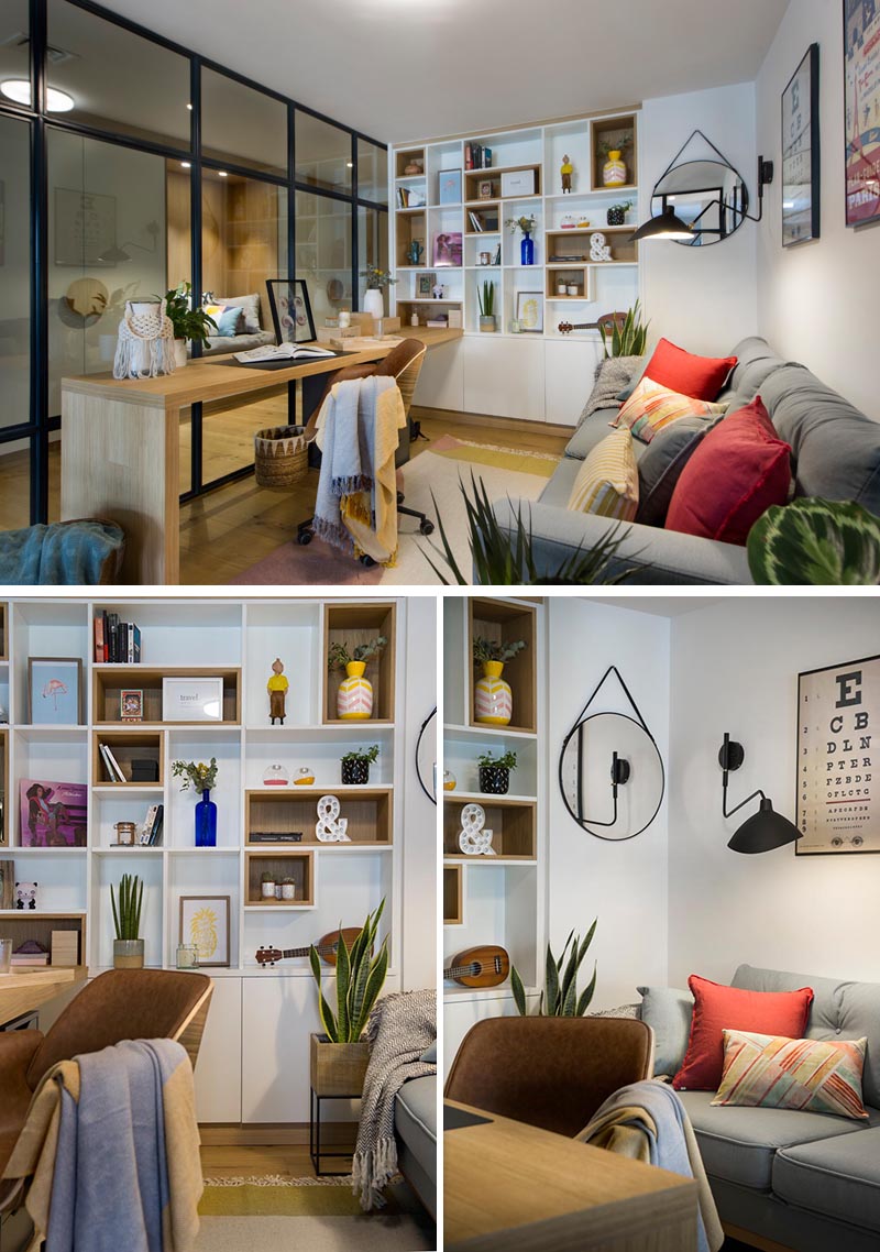 À l'intérieur de ce bureau à domicile vitré moderne se trouve un long bureau en bois qui rencontre une étagère conçue sur mesure, avec certaines des étagères bordées de bois. En face du bureau se trouve un canapé gris confortable, quelques plantes et des oreillers colorés, tandis qu'un tapis ajoute une touche douce sous le pied. #HomeOffice #GlassWalls #Shelving