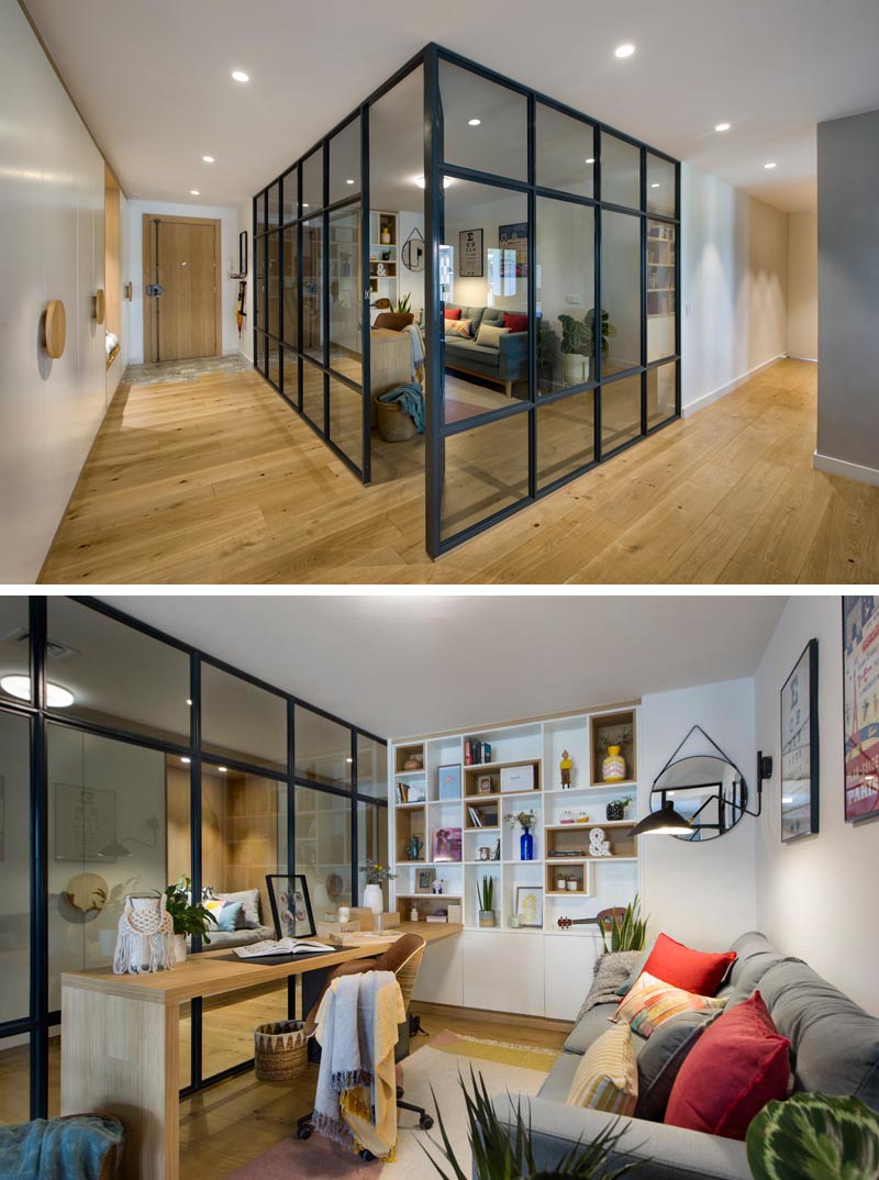 À l'intérieur de ce bureau à domicile vitré moderne se trouve un long bureau en bois qui rencontre une étagère conçue sur mesure, avec certaines des étagères bordées de bois. En face du bureau se trouve un canapé gris confortable, quelques plantes et des oreillers colorés, tandis qu'un tapis ajoute une touche douce sous le pied. #HomeOffice #GlassWalls #Shelving