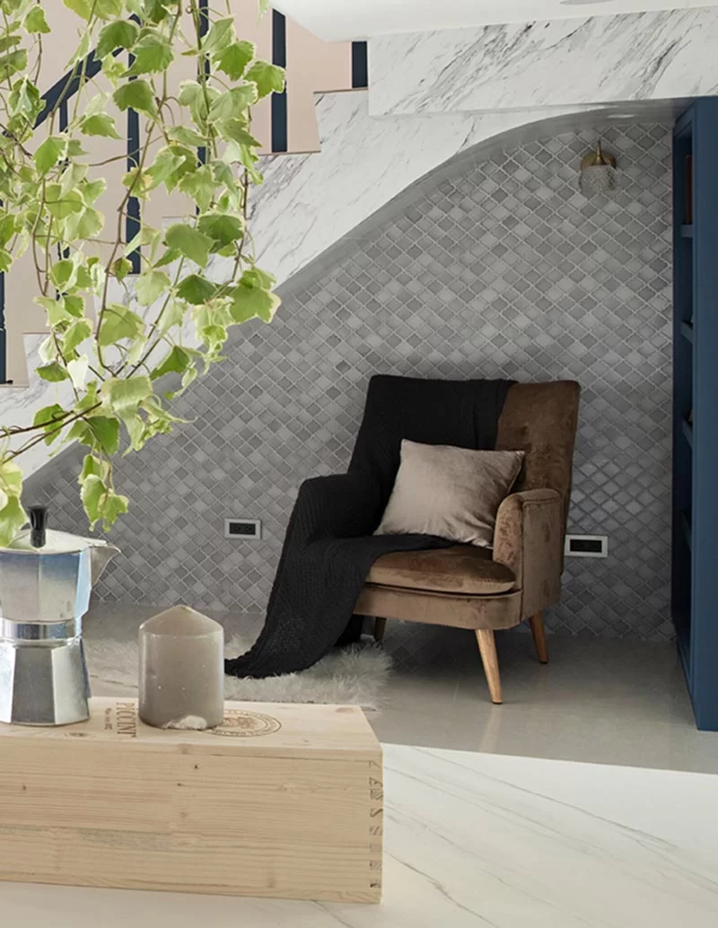 Cette maison moderne dispose d'un petit coin lecture sous l'escalier. Il comprend un mur d'accent en carreaux gris, une étagère bleue personnalisée, un fauteuil confortable, une applique et une paire de prises. #ReadingNook #SeatingNook #UnderStairNook #HomeLibrary