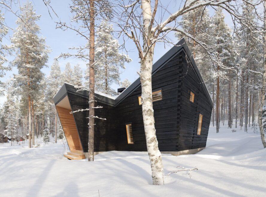 un bâtiment anguleux en bois noir au milieu d'une forêt enneigée