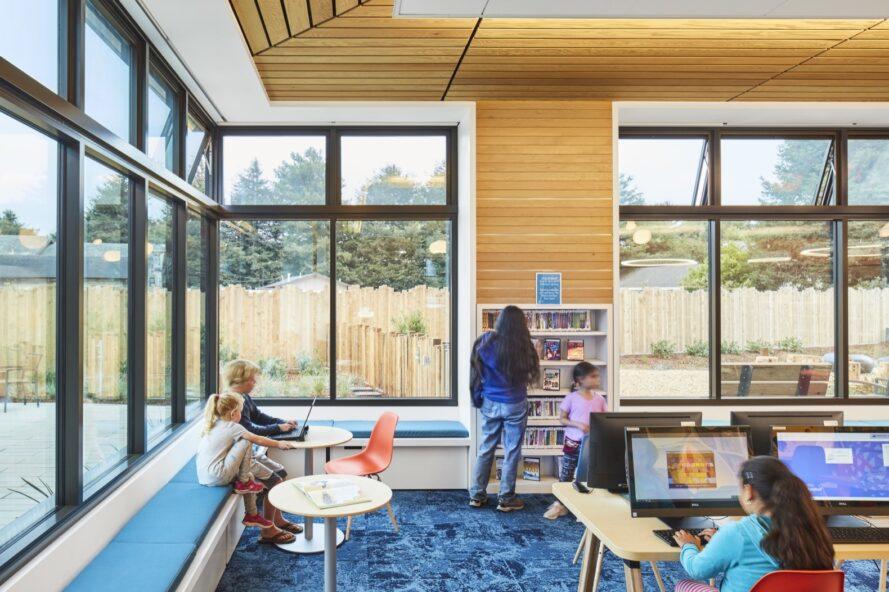 enfants travaillant sur des ordinateurs dans une salle de bibliothèque bleu et blanc