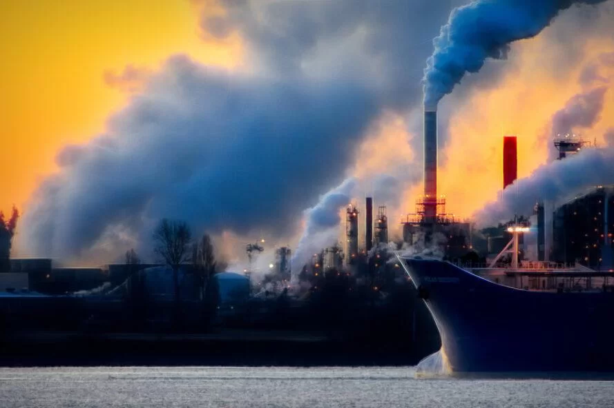 un bateau noir sur l'eau avec une usine derrière elle émettant du gaz dans l'air
