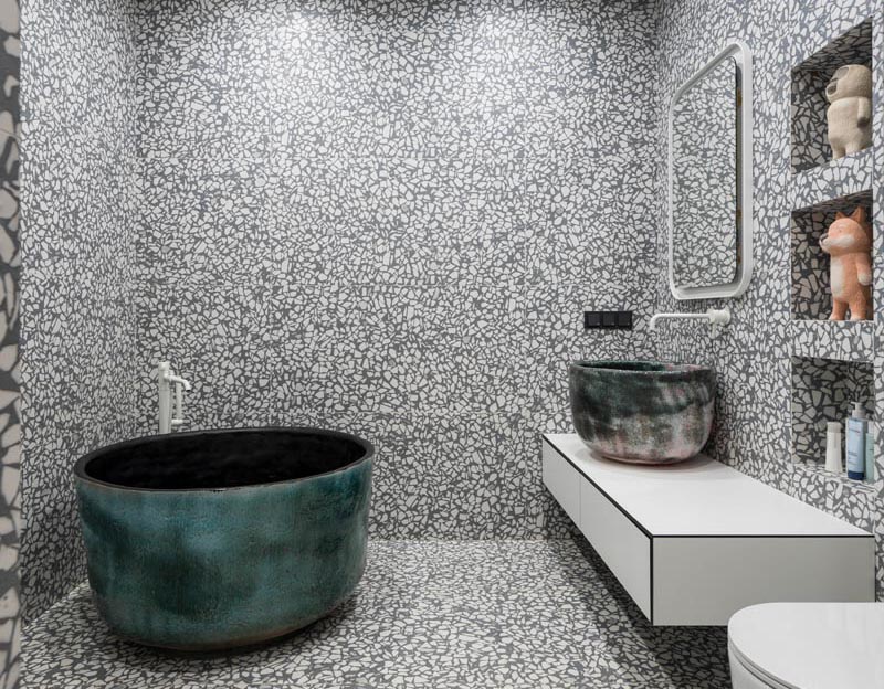 Un grand carreau de terrazzo gris et blanc a été installé dans cette salle de bain moderne, couvrant les murs et le sol. #GreyAndWhiteBathroom #GreyBathroom #BathroomIdeas #SoakingTub #ShelvingNiche #ModernBathroom