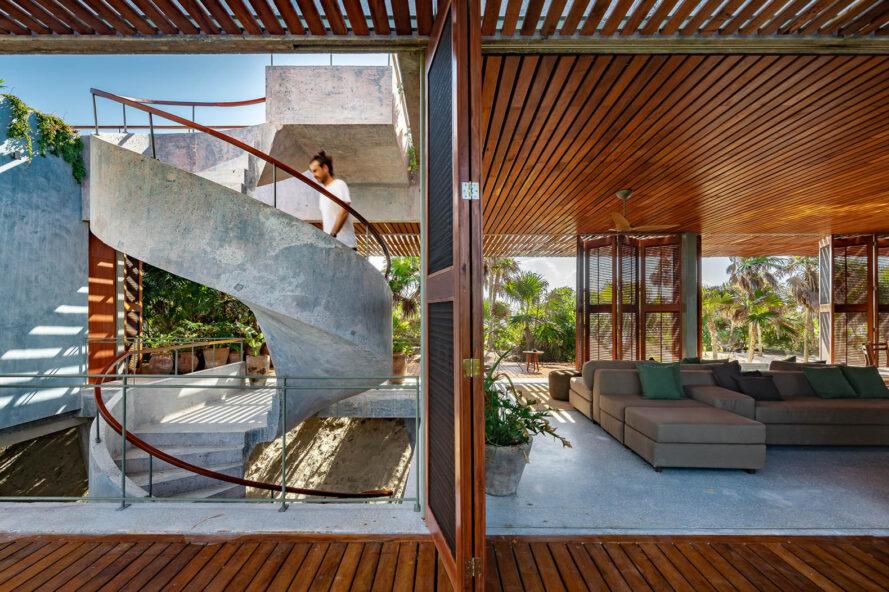 à gauche, un escalier en colimaçon avec une personne qui y monte. à droite, un coin salon dans une structure avec des plafonds en bois et des accents