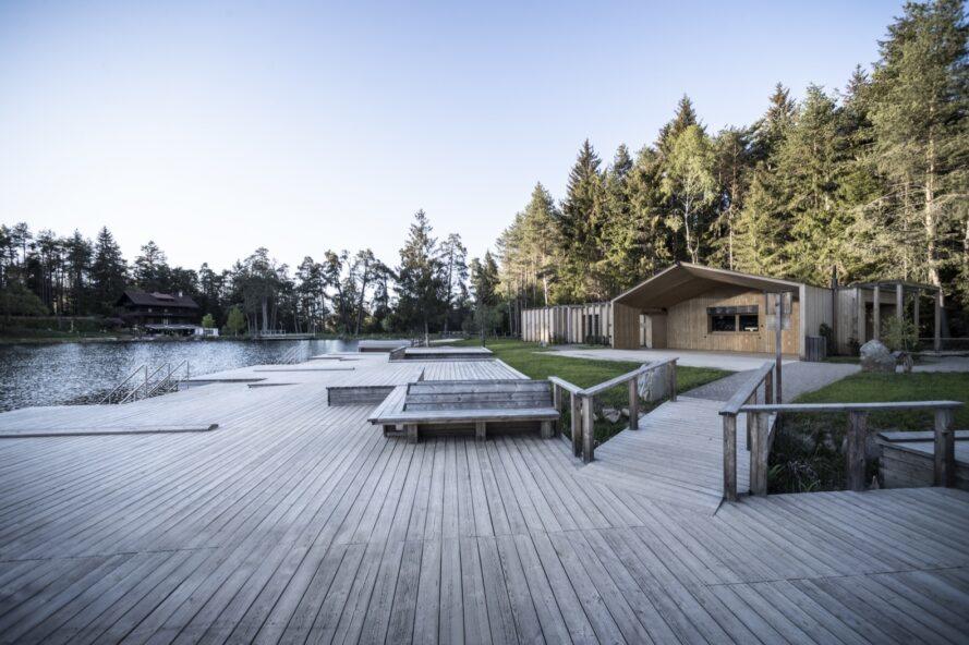 un quai en bois sur un lac, avec une maison au bord du lac et des arbres à droite