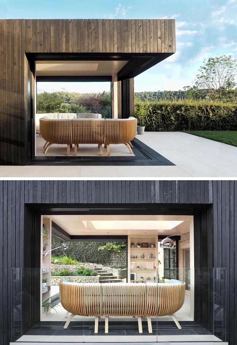 Les portes coulissantes en verre de cette extension moderne disparaissent entièrement derrière trois bibliothèques en bois, qui fournissent également un support vertical à la structure. Lorsqu'elles sont ouvertes, ces portes coulissantes créent un salon extérieur qui s'ouvre sur le jardin. #OutdoorLivingRoom #ModernExtension #HomeOffice #ReadingRoom