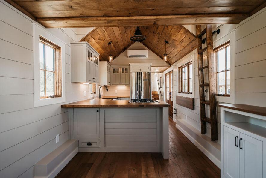 intérieur d'une petite maison avec armoires blanches et plafonds en bois et accents dans la cuisine. une échelle est montée sur le mur