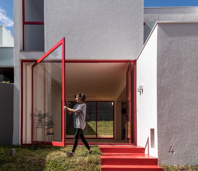 Nommo Arquitetos a récemment terminé la conception d'une maison à Curitiba, au Brésil, qui présente une grande fenêtre pivotante à côté de la porte d'entrée. #PivotingWindow #LargePivotWindow #RedFrontDoor #RedWindowFrames
