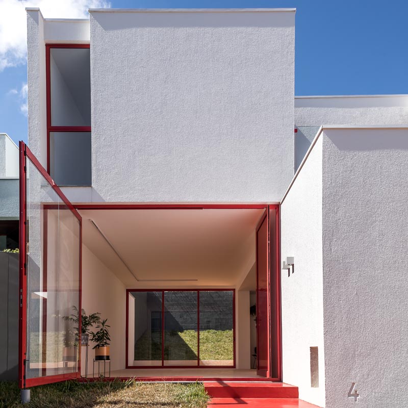 Lorsque la porte d'entrée de cette maison moderne est ouverte, la grande fenêtre pivotante peut être déplacée en poussant le cadre pour l'ouvrir complètement, exposant l'intérieur de la maison au petit patio en herbe. et cour avant. #PivotingWindow #RedFrontDoor #WindowIdeas