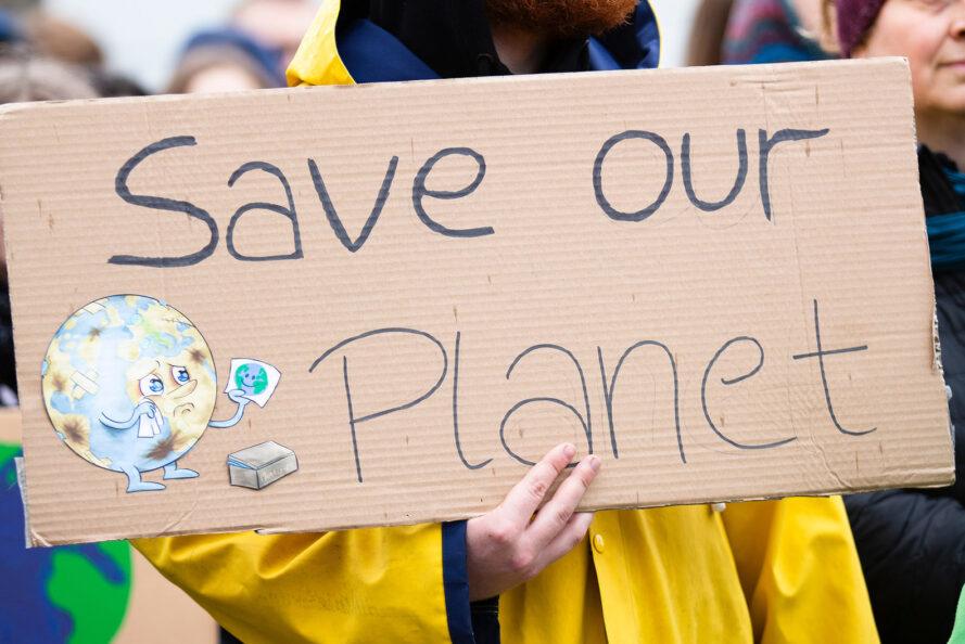 une personne en jaune tenant une pancarte de protestation qui dit "Sauvons notre planète"