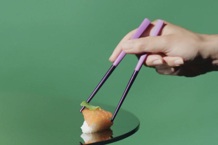 une paire de baguettes violettes ramassant un morceau de sushi.