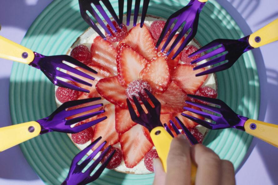dix fourchettes violettes creusant dans une assiette de fraises tranchées.