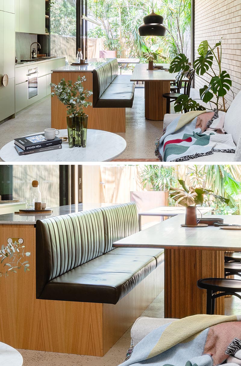 Un îlot de cuisine en bois comprend des banquettes en cuir vert foncé pour la table à manger.